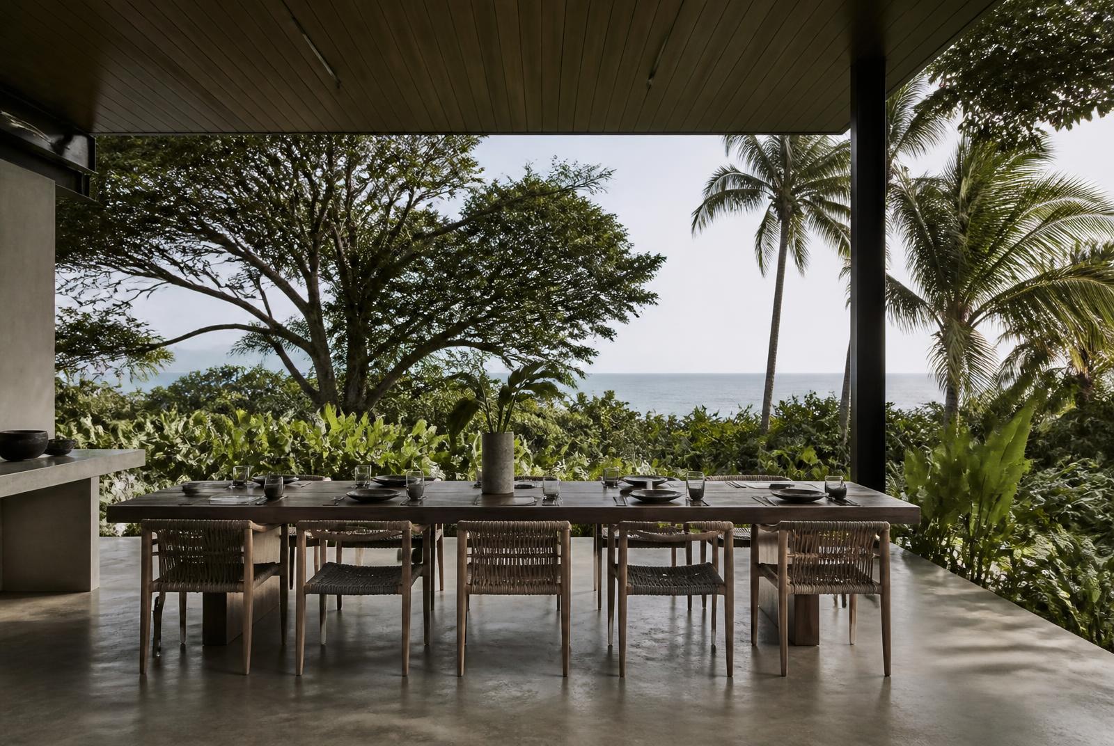 Covered outdoor dining terrace of a Costa Rican house, a long timber table set, tropical greenery beyond.